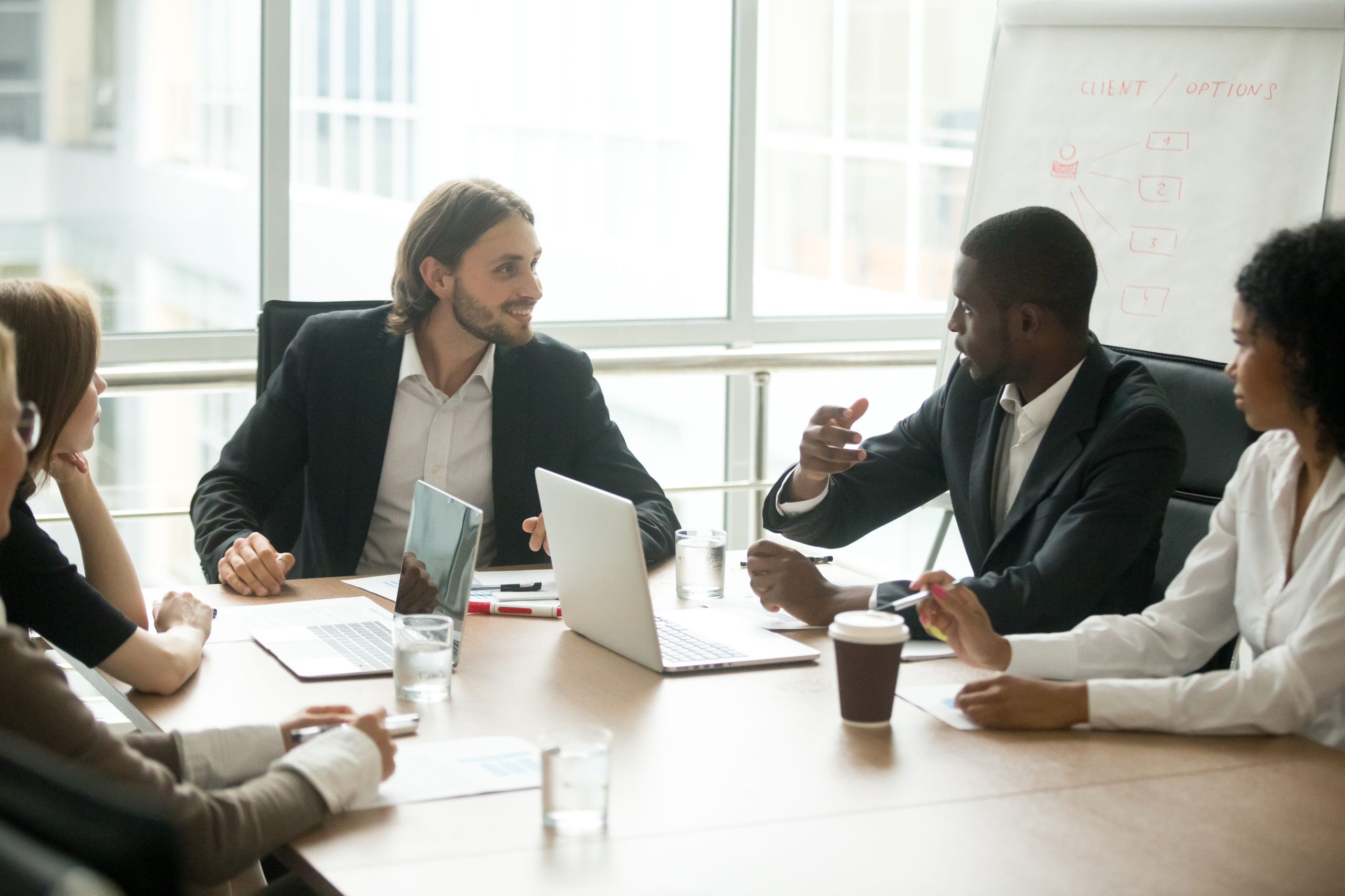 Diverse business executives discussing project sitting at conference table, multiracial partners talking about marketing plan at corporate briefing, african manager offering new idea at group meeting